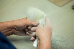A person's hands holding and combing a tuft of white bristles with a small, flat tool on a light-colored surface.