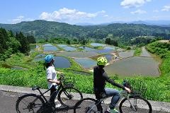 Two people on bicycles admire a scenic view of rice terraces in Yamakoshi, Japan.