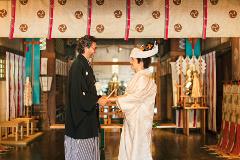 A Japanese couple in traditional wedding attire exchange a celebratory item during a ceremony.