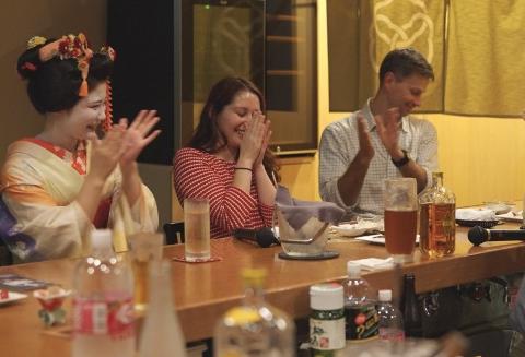 A geisha and two guests clap their hands at a table during an Ozashiki banquet experience.