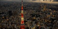 Sunset Departure! Tokyo Helicopter Cruise for 5 – Experience Dusk and Nighttime Cityscapes (Tokyo) An aerial view shows Tokyo Tower illuminated at dusk, surrounded by a dense cityscape of buildings and lights under a cloudy sky.