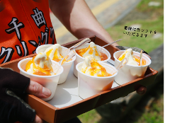 A person's hand holds a tray of several soft-serve ice creams topped with orange sauce.