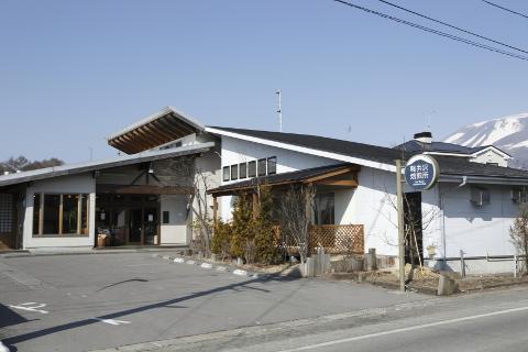 A modern building with a large overhang entrance and a sign for "Karuizawa Coffee" stands under a clear blue sky with a snow-capped mountain in the background.
