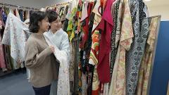 Two women are looking at a collection of kimonos displayed on racks in a shop.