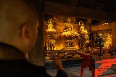 Meisatsu Zojoji Temple - A Journey to Tokyo’s Cultural Origins A monk bows before golden Buddha statues in a dimly lit temple.
