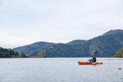 A kayaker paddles across a tranquil lake with tree-covered mountains in the background.