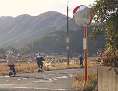 Two people ride electric scooters down a paved road with mountains in the background.
