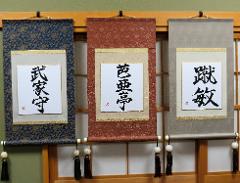 Three decorative scrolls with Japanese calligraphy hang on a wall, each featuring different patterns and characters.
