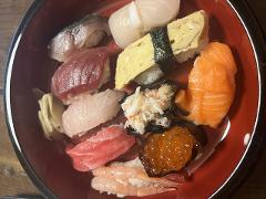 A colorful array of assorted sushi, including salmon, tuna, egg, and roe, is arranged in a red bowl, showcasing a delicious and varied Japanese meal.
