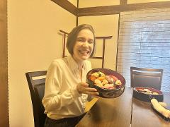 A woman is happily holding a large bowl of sushi while sitting at a table with another bowl of sushi and a side dish.