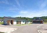 Experience 200 Years of Craftsmanship: Wajima Lacquerware Studio Tour (Visit a craftsman's home) A modern building with a dark roof and white walls sits in a sunny outdoor setting with a clear blue sky and some trees in the background.