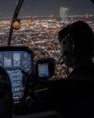 Sunset Departure! Tokyo Helicopter Cruise for 5 – Experience Dusk and Nighttime Cityscapes (Tokyo) A pilot wearing headphones flies a helicopter over a glittering cityscape at night.