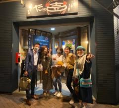 Five people pose in front of "Tarokichi," a bar in Hakodate, Japan, giving thumbs up to the camera.