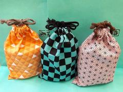Three drawstring pouches with anime patterns are arranged in front of a green background.