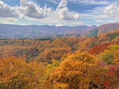 A beautiful mountain landscape covered in vibrant autumn foliage under a cloudy sky.