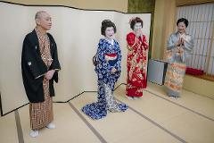 Geisha Ozashiki at Asakusa, a Quality Time Filled with Art and Japanese Culture Four individuals in traditional Japanese attire, including two geishas, stand in a room with tatami flooring and shoji screens.