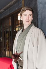 Asakusa Kimono Rental Plan - Choose From a Variety of Beautiful Kimonos A person in traditional Japanese attire stands against a textured wall, with a red carpet visible in the foreground.