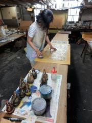 A person is creating a Yuzen scarf by hand at a workbench in a workshop.