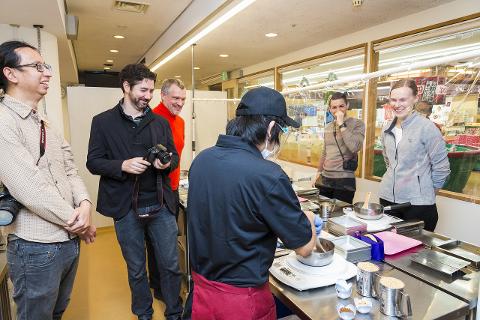 A group of people in a kitchen in Asakusa, Japan, observe a chef making traditional Japanese snacks.