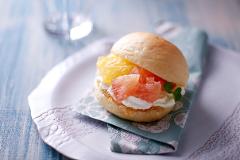 Gros plan d&#39;un sandwich sucré rempli d&#39;agrumes et de crème blanche, orné d&#39;une feuille de menthe, posé sur une serviette à motifs posée sur une assiette blanche décorative.