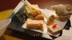 A platter of meticulously arranged small Japanese dishes, including a layered jelly with salmon, fried morsels, and a sea snail, awaits diners.