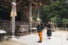 Two people, one with a backpack and the other with a scarf, pray at a Japanese temple.