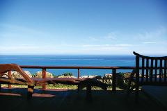 Seascape view from a shaded wooden deck with rustic wooden benches.
