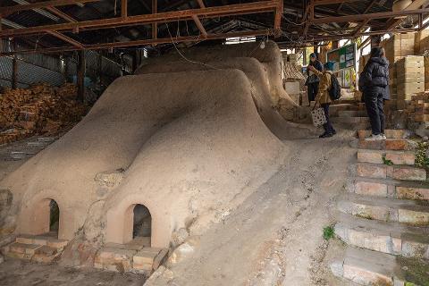 Ceramică și porțelan: Povești ale artizanilor din spatele meșteșugului A tall, slender turquoise vase with a glossy finish sits on a wooden surface against a light grey wall.