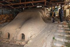 Ceramică și porțelan: Povești ale artizanilor din spatele meșteșugului A tall, slender turquoise vase with a glossy finish sits on a wooden surface against a light grey wall.