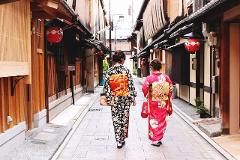 Two women in traditional kimonos walk away from the camera down a narrow, traditional Japanese street.