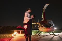 Sunset Departure! Tokyo Helicopter Cruise for 5 – Experience Dusk and Nighttime Cityscapes (Tokyo) A man lifts a woman into his arms with a helicopter behind them at night.