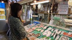 En kvinde køber fisk og skaldyr på et marked i Hakodate, Japan, og undersøger de friske fisk og skaldyr, der er udstillet.