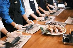People in aprons and gloves prepare fish on a wooden table.