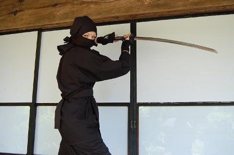 一个打扮成忍者的人手持武士刀站在窗前。