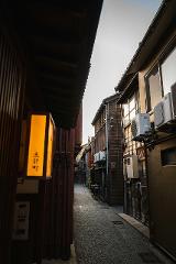 A narrow alleyway lined with traditional Japanese wooden buildings and illuminated by a warm, glowing lantern.
