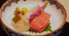This image shows a beautifully arranged plate of sashimi with pink flowers, wasabi, and ginger, presented in an ornate bowl.
