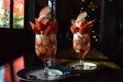 Two elegant strawberry parfaits topped with whipped cream and sliced strawberries are displayed on plates in a dimly lit setting.