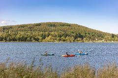 Visit the Spring Water Flowing into Lake Shirakaba and Experience the Origins of Our Connection with Nature – Private Guided Canoe Tour People kayak on a lake with a tree-covered hill in the background.