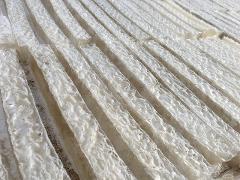 Rows of translucent, textured strands of agar are laid out on a surface, likely drying in the sun.