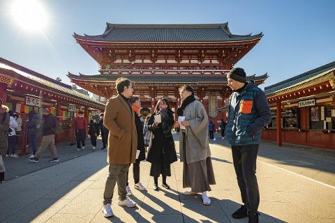 A group of tourists stand in front of a temple in Japan, with the sun shining brightly.