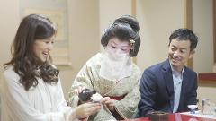 Geisha Ozashiki at Asakusa, a Quality Time Filled with Art and Japanese Culture A woman in traditional geisha attire pours sake into a cup for a smiling couple in a formal setting.