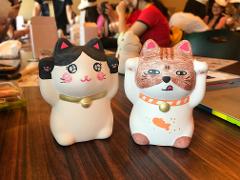 Two ceramic lucky cats, one black and white and the other brown and white, sit on a wooden table.