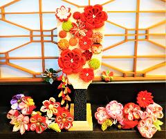 Traditional Japanese Craft Experience -- "Tsumami-Zaiku" Accessory A display of vibrant, handcrafted fabric flowers in traditional Japanese tsumami-zaiku style, set against a backdrop of wooden lattice work.