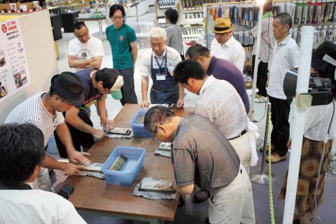 A group of people is gathered around a table, learning how to sharpen knives with a demonstration by an instructor in a store with knives and other products in the background.