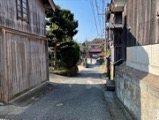 A narrow street lined with traditional wooden buildings leads uphill through a Japanese fishing town.