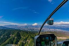 Private Helicopter Tour of Tokyo View of Mount Fuji from a helicopter cockpit overlooking lush green mountains and a city on a clear day.