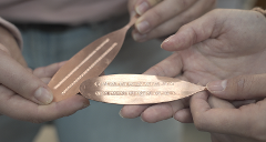 Two hands hold two oval copper metal pieces with intricate etched patterns.