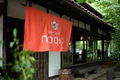 Geleneksel ahşap çerçeveli girişinin dışında, modern bir logonun yer aldığı parlak turuncu bir pankart asılı olan bir Japon restoranı.