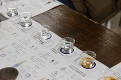 A tasting of sake is arranged on a paper mat with information about each variety, alongside several small glasses of sake and a dark wooden table.