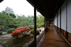 A scenic view from a Japanese-style hallway of a castle and garden with red flowers.